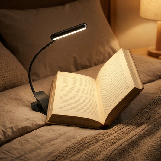 Luz de lectura con pinza encendida sobre un libro en la cama